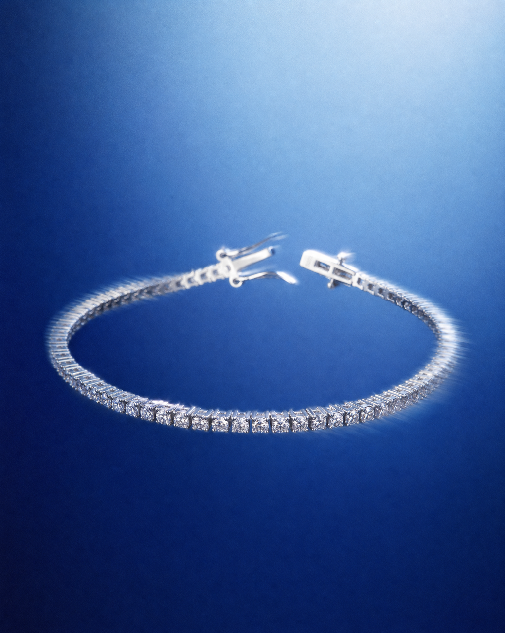 A silver tennis bracelet with a continuous row of clear stones, displayed against a blue gradient background.